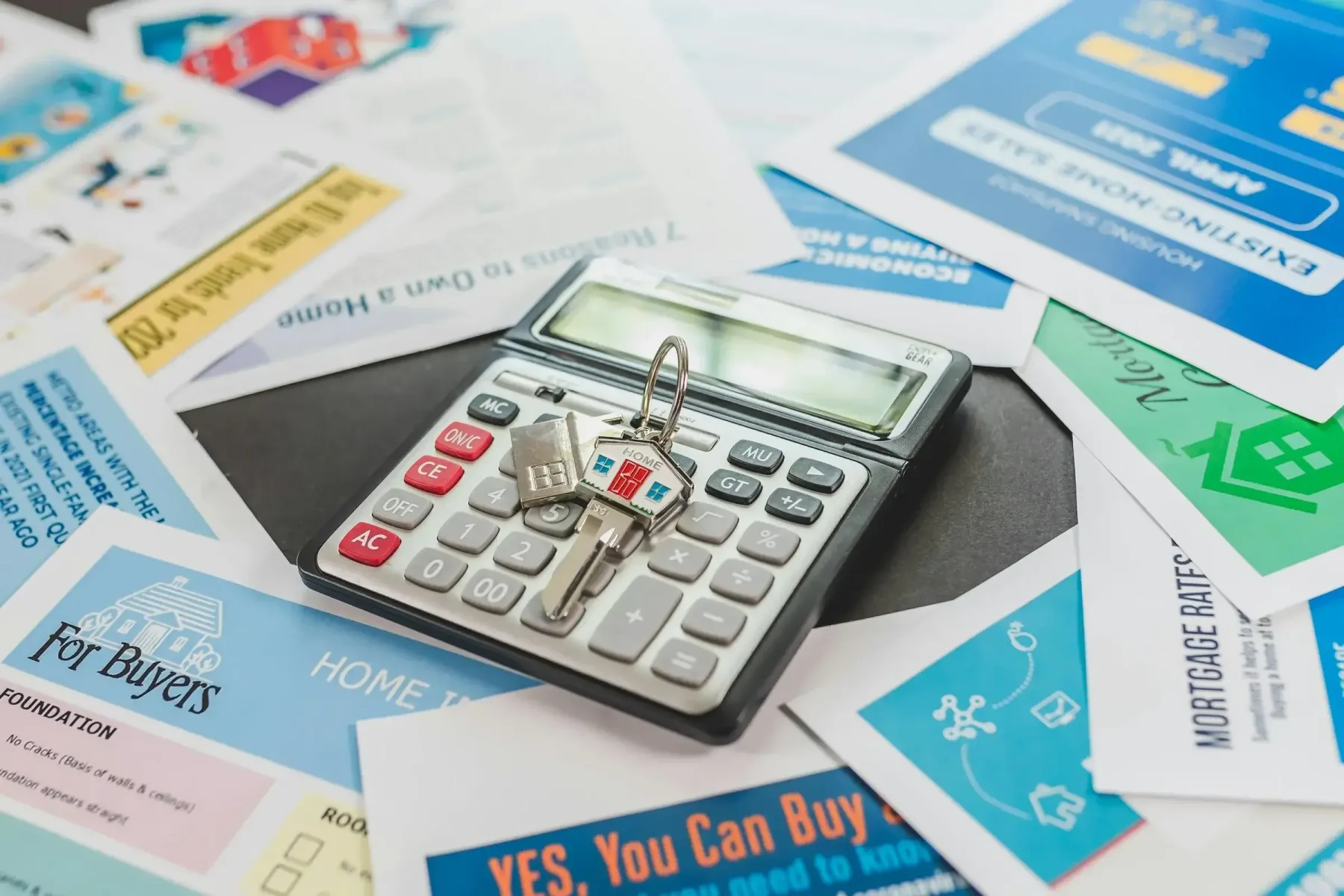 Calculator and house keys on top of real estate flyers